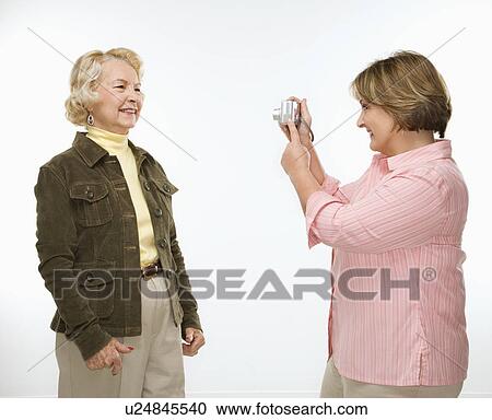 Stock Image - Middle aged woman taking photo of senior woman with digital camera.. Fotosearch