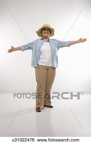 Stock Photograph - Middle aged woman wearing straw hat holding arms outstretched. Fotosearch