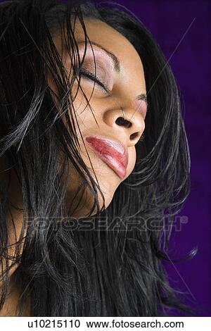 Stock Image - Portrait of mid-adult African American woman against purple background. . Fotosearch