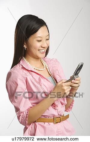 Stock Image - Portrait of mid-adult female smiling and text messaging on cell phone. Fotosearch