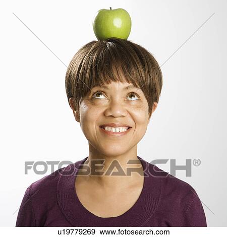 Portrait of middle-aged woman balancing green apple on head looking up and smiling View Large Photo Image Stock Photo - Portrait of middle-aged woman balancing green apple on head looking up and smiling. Fotosearch