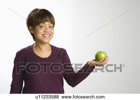 Stock Photo - Portrait of woman holding green apple smiling and looking at viewer. Fotosearch
