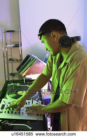 Stock Photography - Profile of young DJ with mixing equipment, turntables and headphones.. Fotosearch