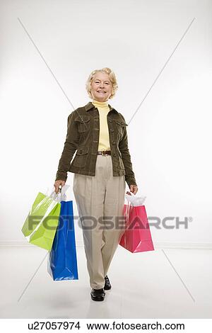Picture - Senior woman holding gift bags smiling at viewer. Fotosearch