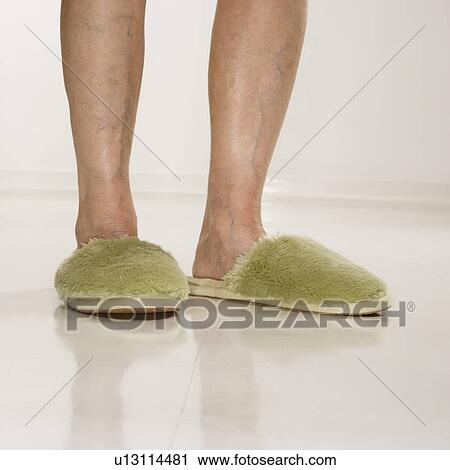 Stock Image - Senior woman's feet wearing green bedroom slippers.. Fotosearch
