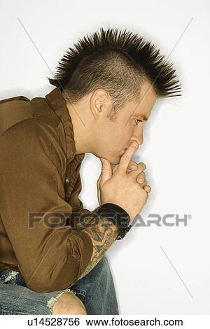 Stock Photograph - Side view of man with mohawk sitting with hands to face against white background. Fotosearch