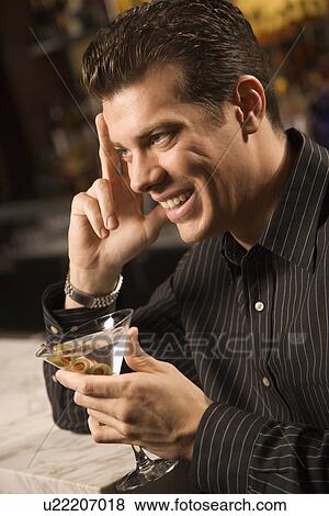 Stock Photo - Side view of mid adult man holding martini with hand to head smiling. Fotosearch