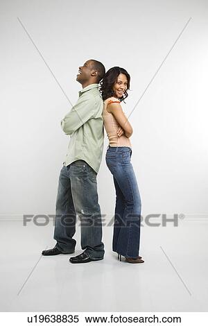 Stock Photography - Studio shot of couple standing back to back with arms crossed and smiling. Fotosearch
