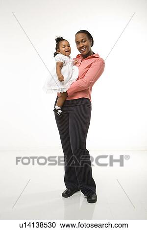 Stock Image - Woman holding infant girl standing against white background. Fotosearch