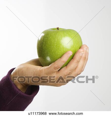 Stock Photo - Woman holding out green apple in hand. Fotosearch
