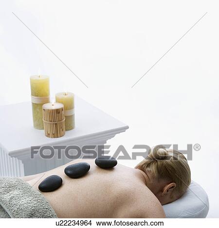Woman lying on massage table with hot stones on her back View Large Photo Image Picture - Woman lying on massage table with hot stones on her back. Fotosearch
