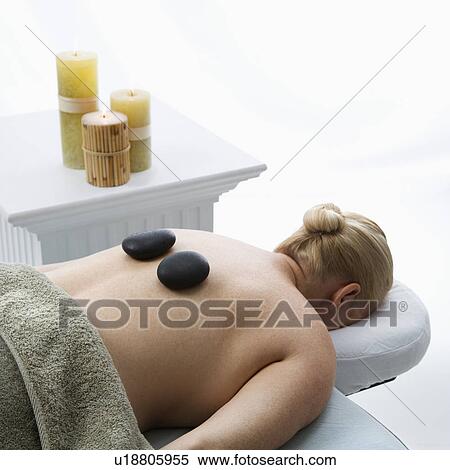 Stock Photography - Woman lying on massage table with hot stones on her back. Fotosearch