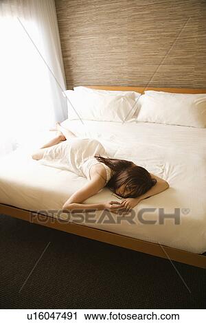 Stock Image - Woman wearing nightgown lying on bed. Fotosearch