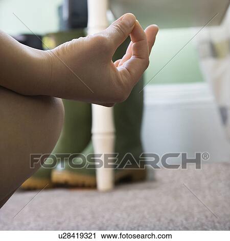 Stock Image - Woman's hand resting on her knee with fingers in meditation pose. Fotosearch
