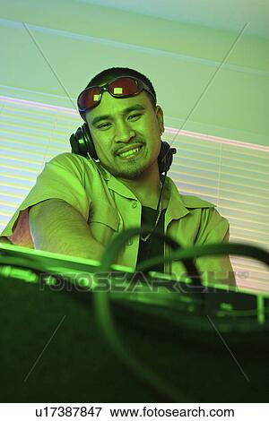 Stock Photo - Young adult DJ behind mixing equipment looking at viewer smiling. Fotosearch