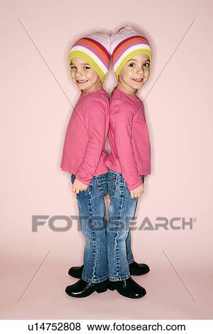 Young female twin girls standing back to back. View Large Photo Image Stock Photo - Young female twin girls standing back to back.. Fotosearch