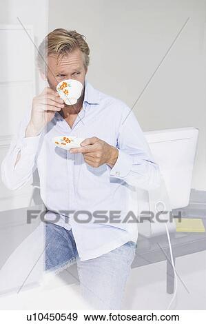 Stock Photo - Man in office drinking cup of tea with reflections.. Fotosearch