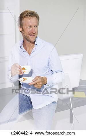 Picture - Man in office with cup of tea smiling with reflections.. Fotosearch