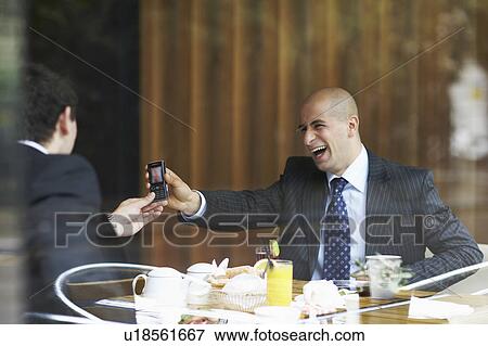 Stock Photo - Two businessmen in a restaurant looking at a cell phone. Fotosearch