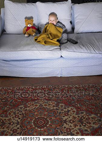 Stock Image - Baby (1-3 months) watching television on sofa with teddy bear. Alicante, Spain.. Fotosearch