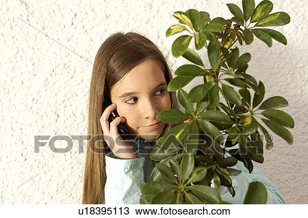 Girl (12-14) using mobile phone hiding behind plant View Large Photo Image Stock Image - Girl (12-14) using mobile phone hiding behind plant. Fotosearch