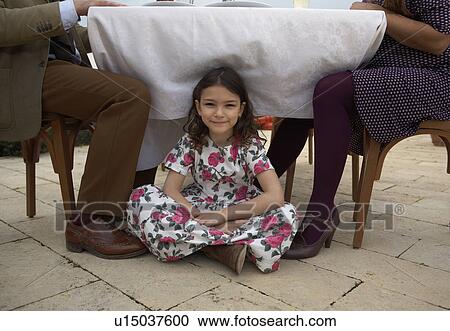 Stock Image - Girl (9-11) sitting under family table, portrait. Fotosearch