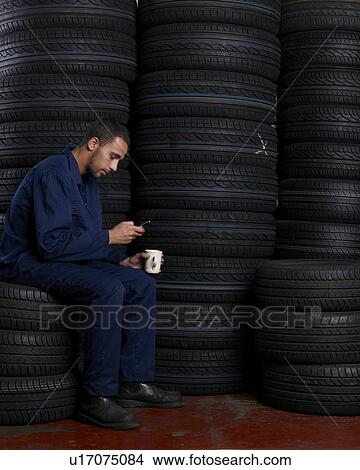 Picture - Mechanic sitting on a stack of tires. Fotosearch