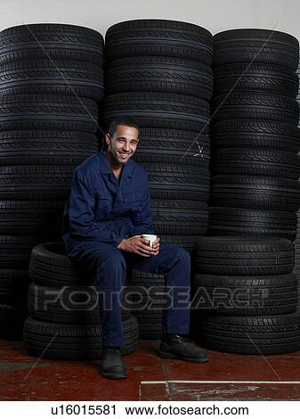 Stock Image - Mechanic sitting on a stack of tires. Fotosearch