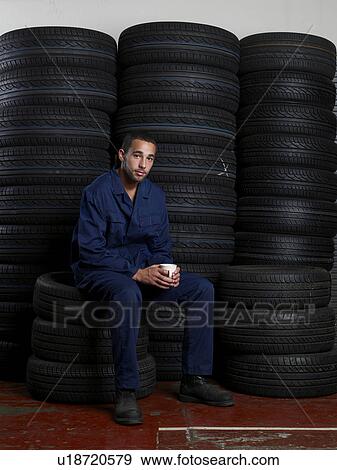 Stock Photo - Mechanic sitting on a stack of tires. Fotosearch