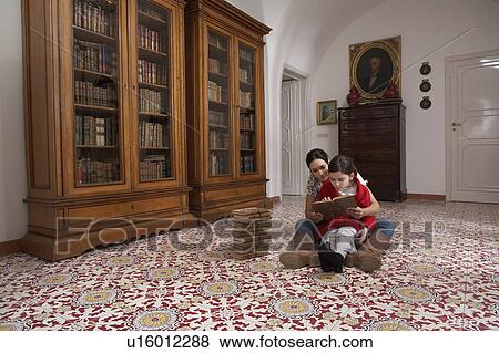 Stock Photo - Mother and daughter (5-7) sitting on floor reading books. Fotosearch