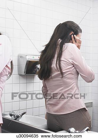 Woman reflected in office washroom mirror using mobile phone View Large Photo Image Stock Photography - Woman reflected in office washroom mirror using mobile phone. Fotosearch