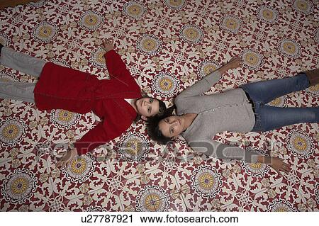 Stock Image - Young woman and daughter (9-11) lying on tiled floor, portrait. Fotosearch