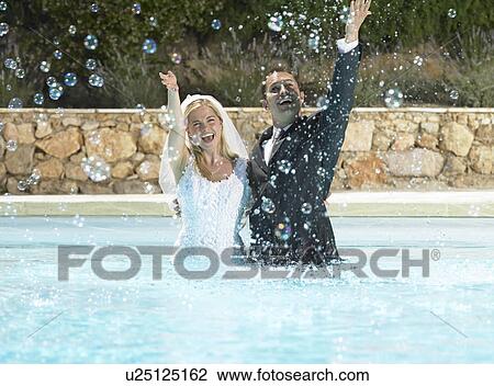 Stock Image - Bride and groom splashing in pool. Fotosearch