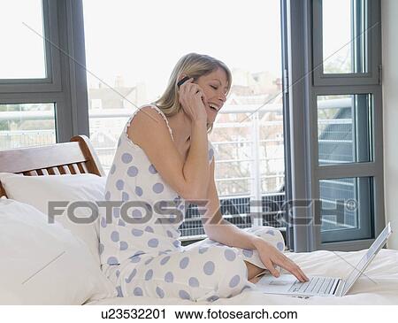 Stock Image - Female working from home in bed. Fotosearch