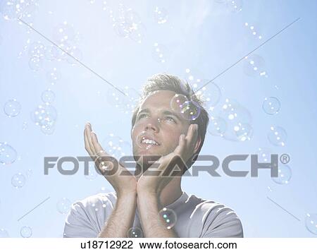 Stock Image - Man in sun holding bubbles. Fotosearch