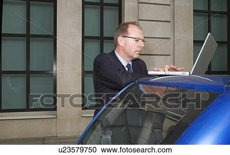 Stock Image - Man using laptop on car. Fotosearch