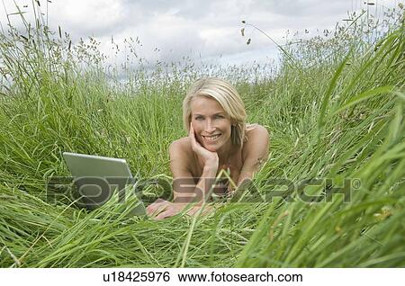 Stock Photograph - Woman lying in field with laptop. Fotosearch