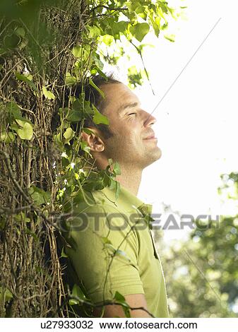 Stock Image - Young man leaning against tree. Fotosearch