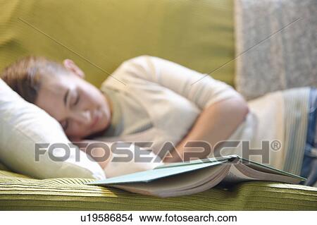 Picture - Young woman lying on couch, with book. Fotosearch
