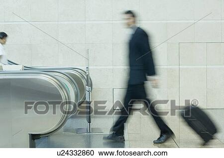 Stock Image - Blurred view of a businessman carrying his luggage. Fotosearch
