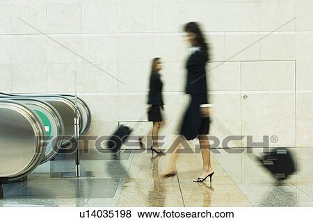 Stock Photo - Blurred view of two businesswomen carrying their luggage. Fotosearch