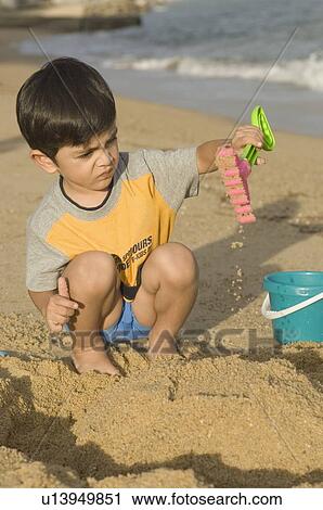 Stock Image - Boy playing with a sand pail and a shovel on the beach. Fotosearch