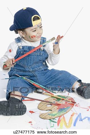 Stock Photography - Boy sitting and looking at a paintbrush. Fotosearch