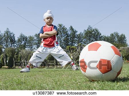 Stock Photo - Boy standing behind a soccer ball with his arms crossed. Fotosearch