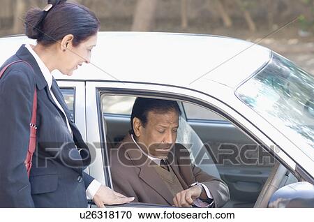Businessman checking the time in a car with a businesswoman standing beside him View Large Photo Image Stock Image - Businessman checking the time in a car with a businesswoman standing beside him. Fotosearch