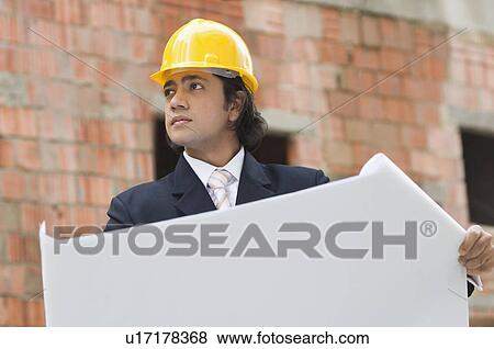 Stock Photo - Businessman holding a blueprint and looking away. Fotosearch