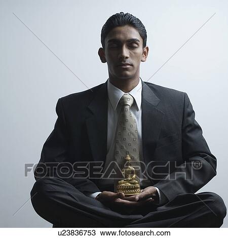 Stock Image - Businessman meditating beside a Buddha statue. Fotosearch