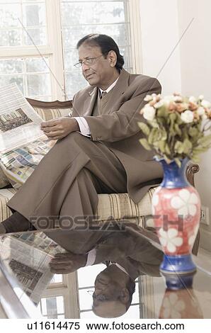 Businessman sitting on a couch and reading a newspaper View Large Photo Image Stock Photography - Businessman sitting on a couch and reading a newspaper. Fotosearch