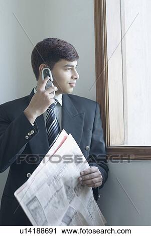 Businessman talking on a mobile phone and holding a newspaper View Large Photo Image Stock Image - Businessman talking on a mobile phone and holding a newspaper. Fotosearch