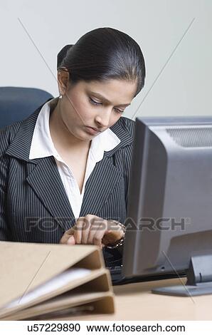 Stock Image - Businesswoman checking the time in front of a computer. Fotosearch